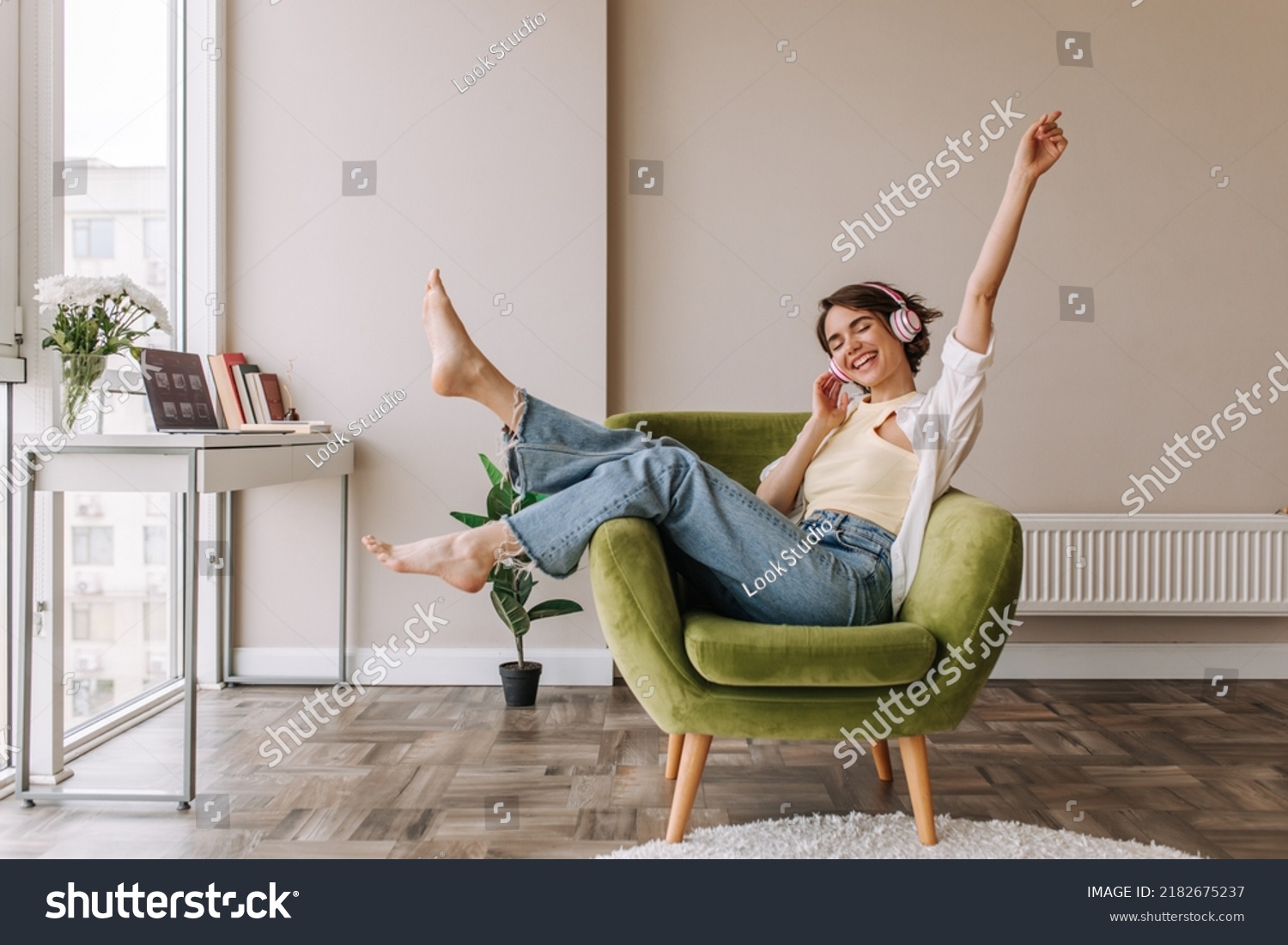 Caucasian beautiful woman smiling at home in headphones . Short brunette hair young girl wearing blue jeans listen music at home. Use technology, lifestyle concept  #2182675237