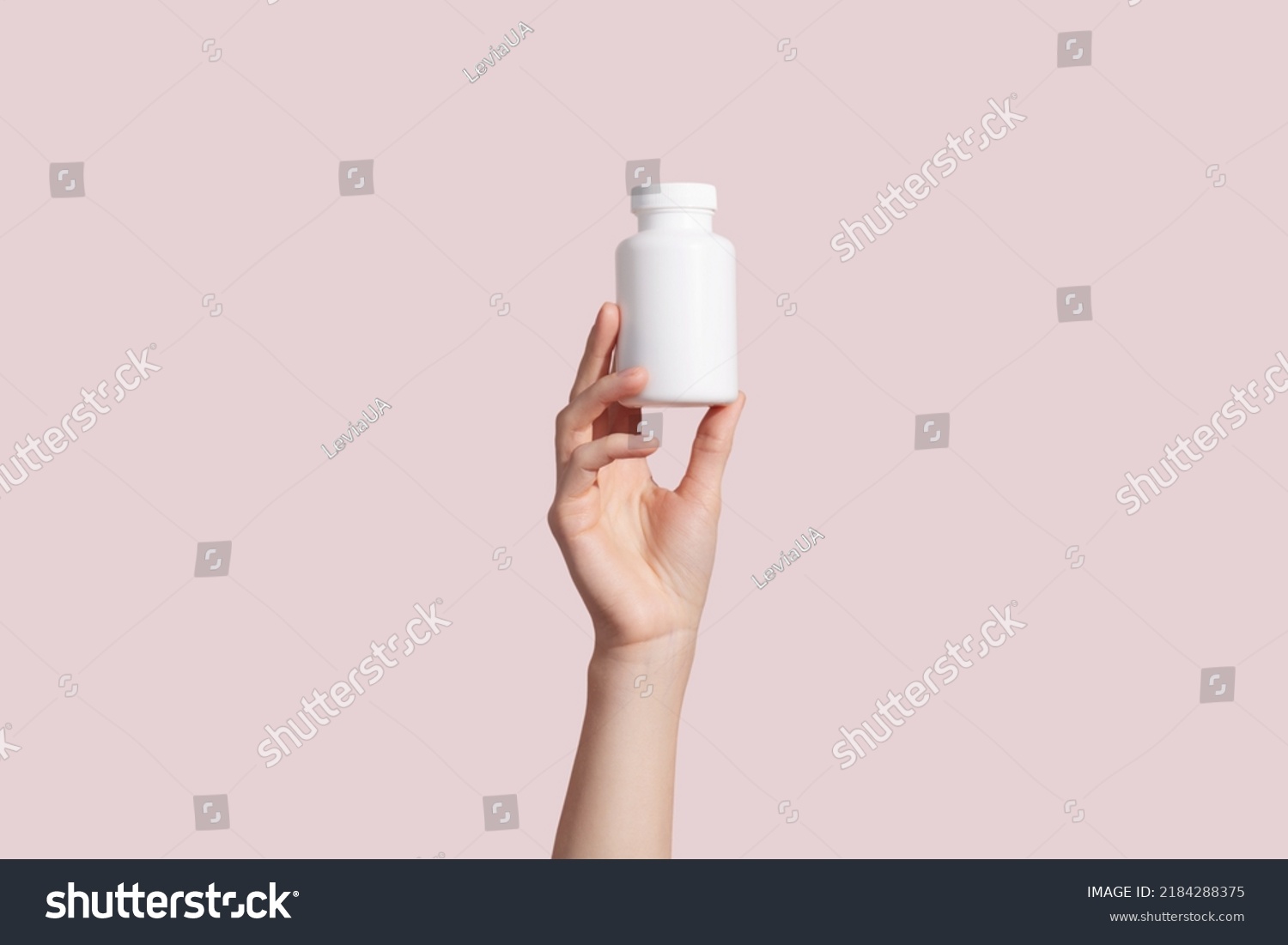 Young female hand holding blank white squeeze bottle plastic tube on pink background. Packaging for pill, capsule or supplement. Product branding mockup. High quality photo #2184288375