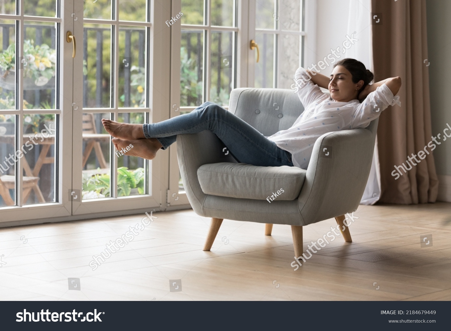Calm peaceful lazy young Indian homeowner woman resting in armchair with closed eyes at big terrace window, breathing fresh cool air, enjoying peace, leisure, comfort, meditating at home #2184679449