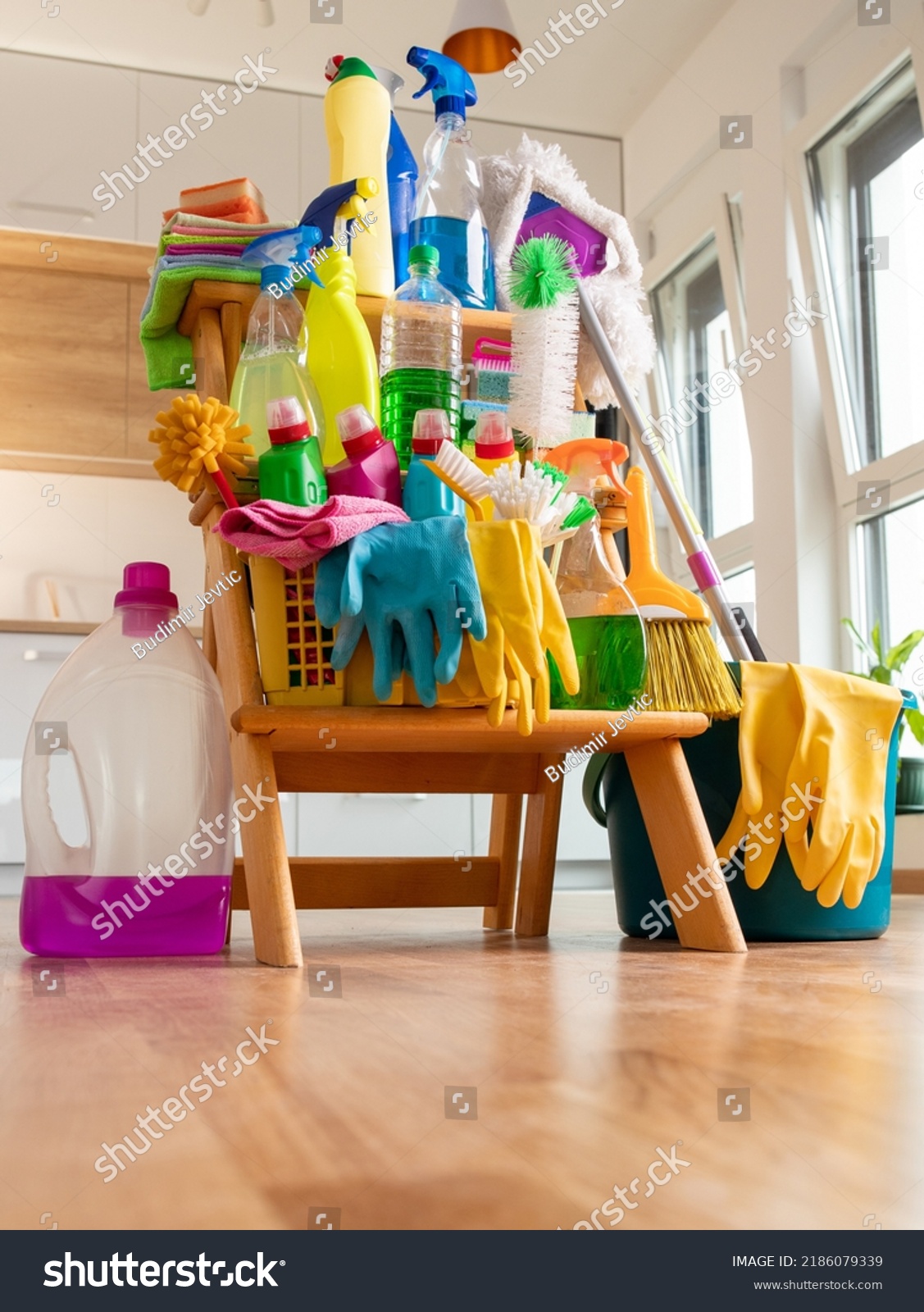 Close up of cleaning products arranged on wooden shelves in front of kitchen. Housekeeping concept #2186079339