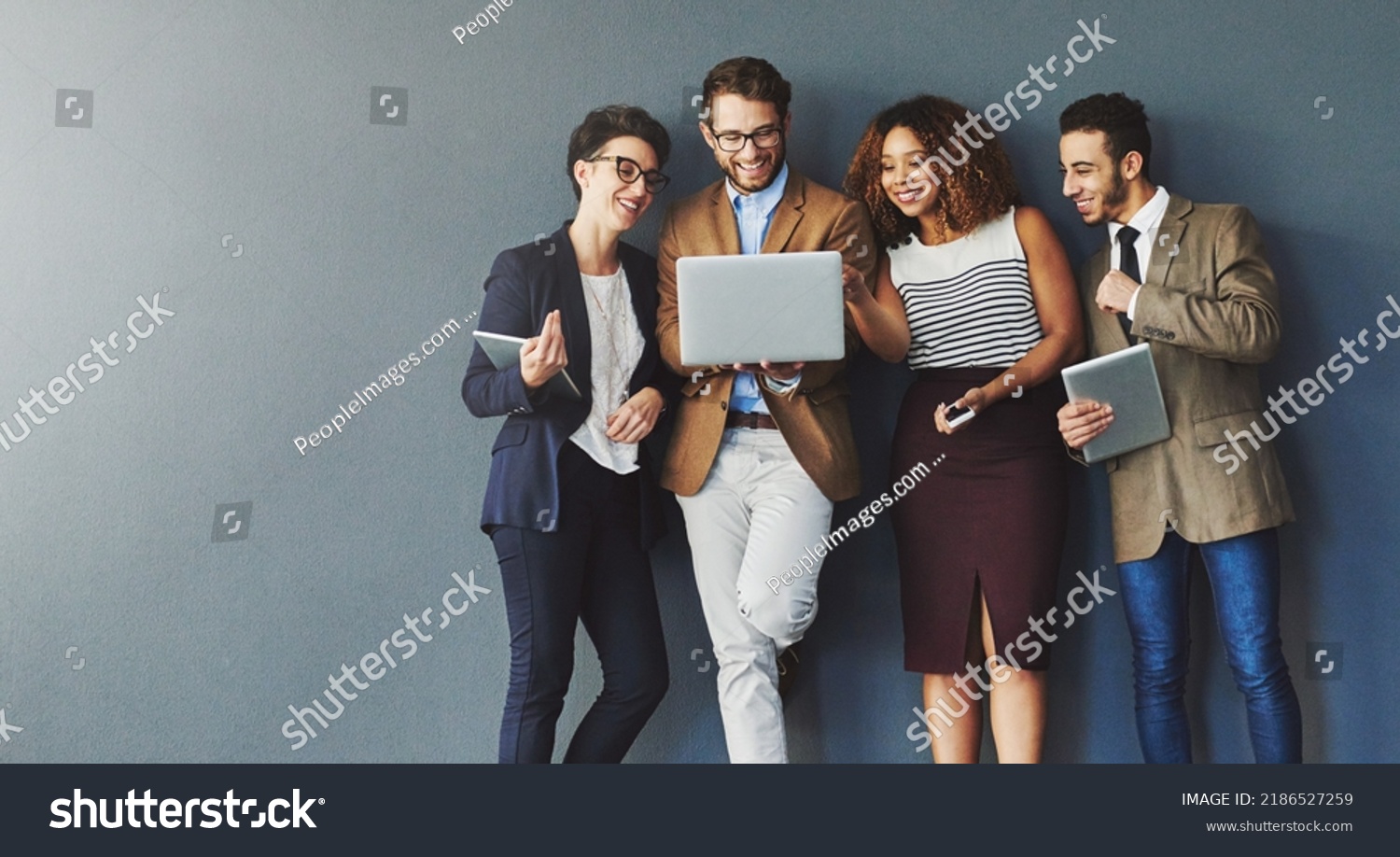 Diverse group of business people with technology browsing, searching and reading positive online reports, data or charts on laptop. Team of creative marketing agents against grey wall with copy #2186527259