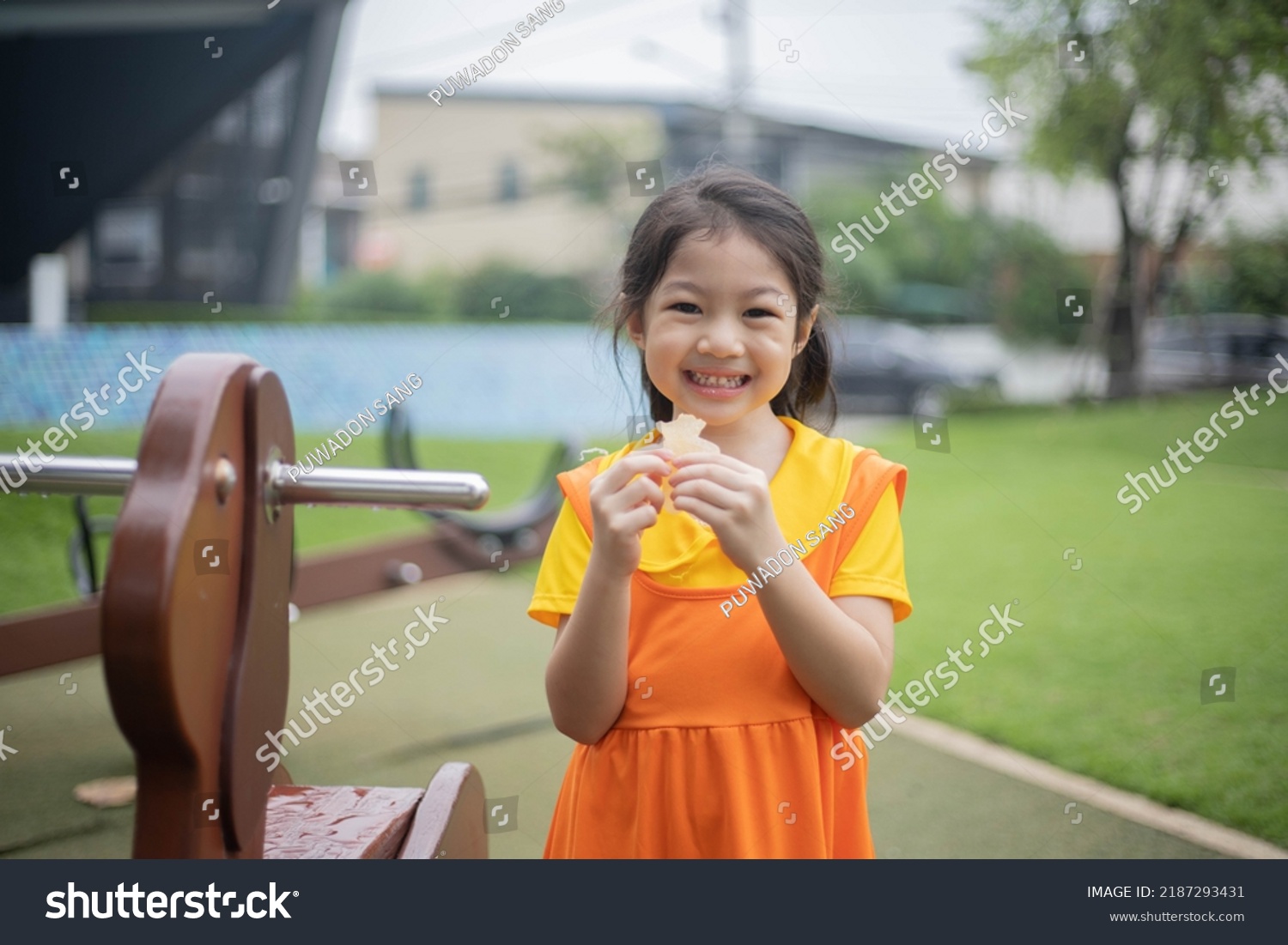 Happy asian girl in orange dress eating jelly candy. #2187293431