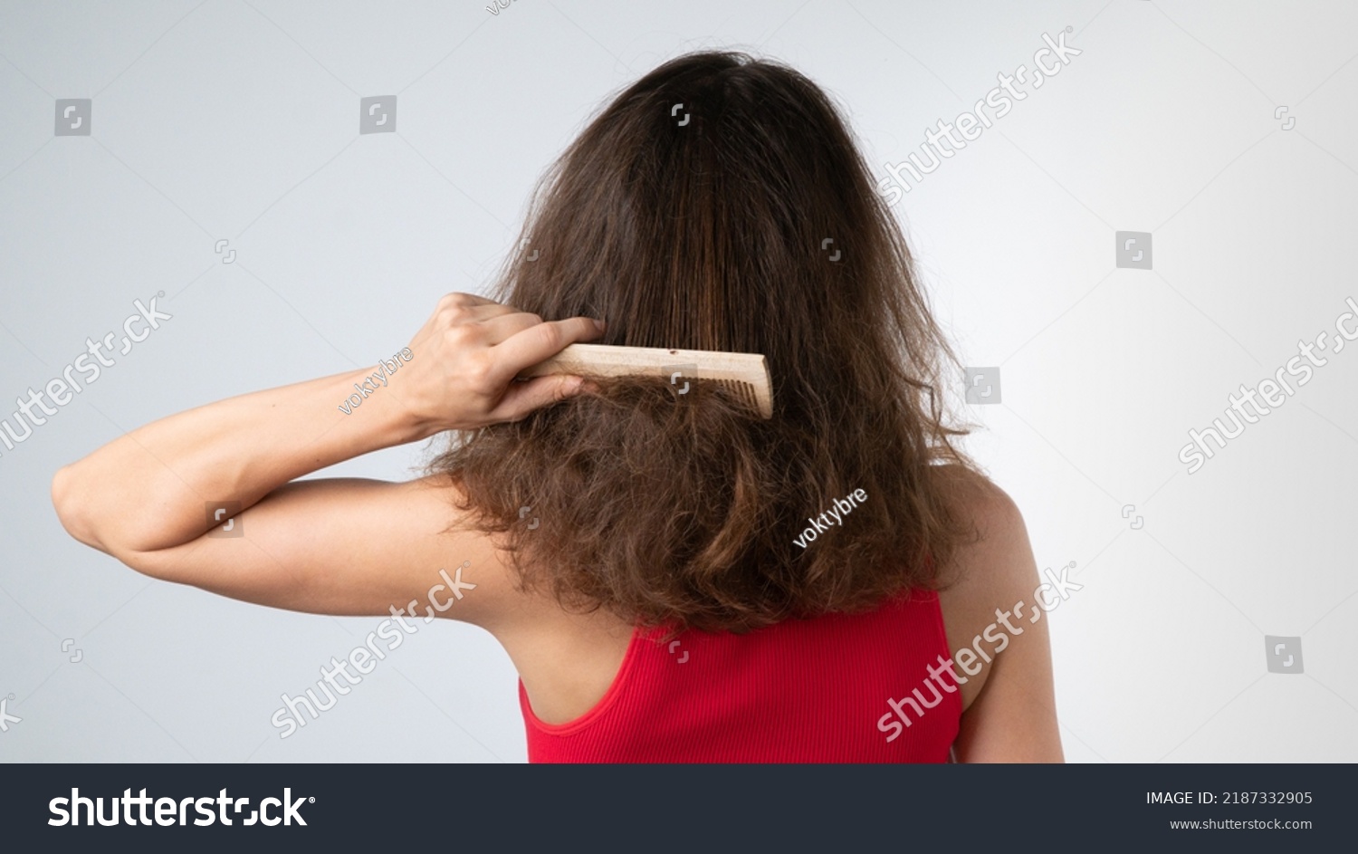 A woman tries to comb her tangled hair from behind with a comb - hair problems. High quality photo #2187332905