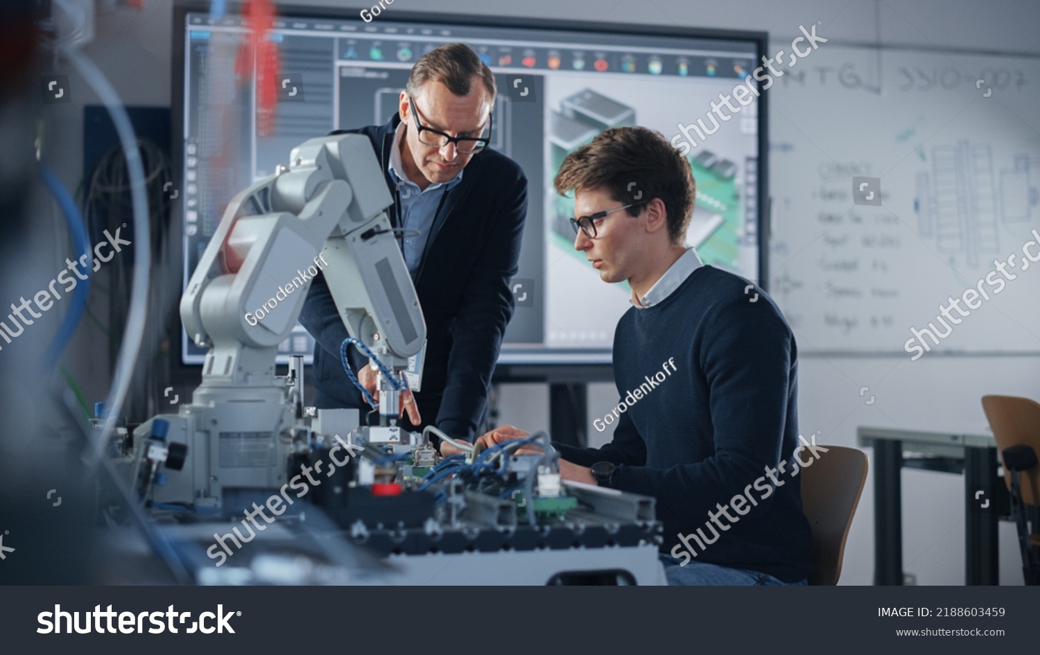Product Supervisor Consults Young Engineer Working with Optimization of Robot Arm. People Doing Robotic Hand Maintenance Ideas. High-Tech Science and Engineering Concept. Medium Shot #2188603459