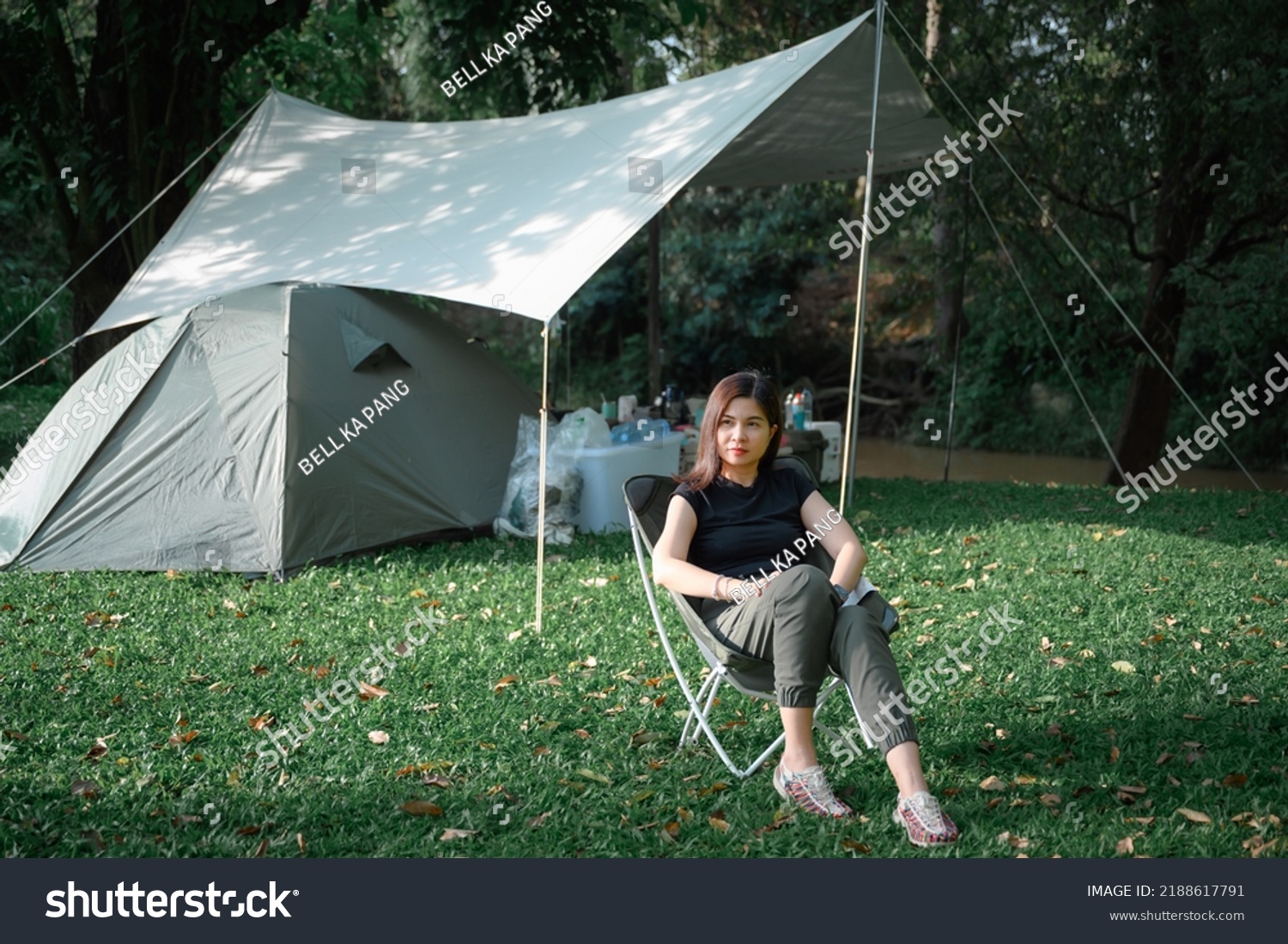 Asian woman sitting on a lawn chair rest on vacation Female tourists like to travel and go camping. pitch a tent and sleep in the natural forest #2188617791