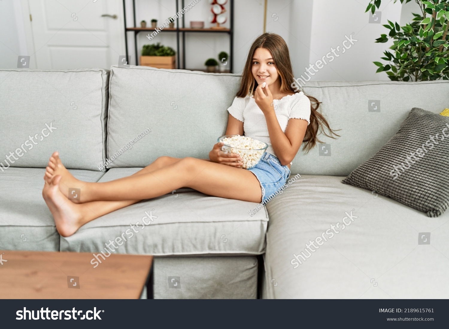 Adorable girl watching movie sitting on sofa at home #2189615761