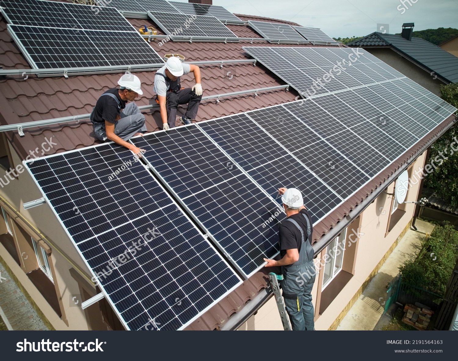 Men installers mounting photovoltaic solar moduls on roof of house. Engineers in helmets installing solar panel system outdoors. Concept of alternative and renewable energy. Aerial view. #2191564163