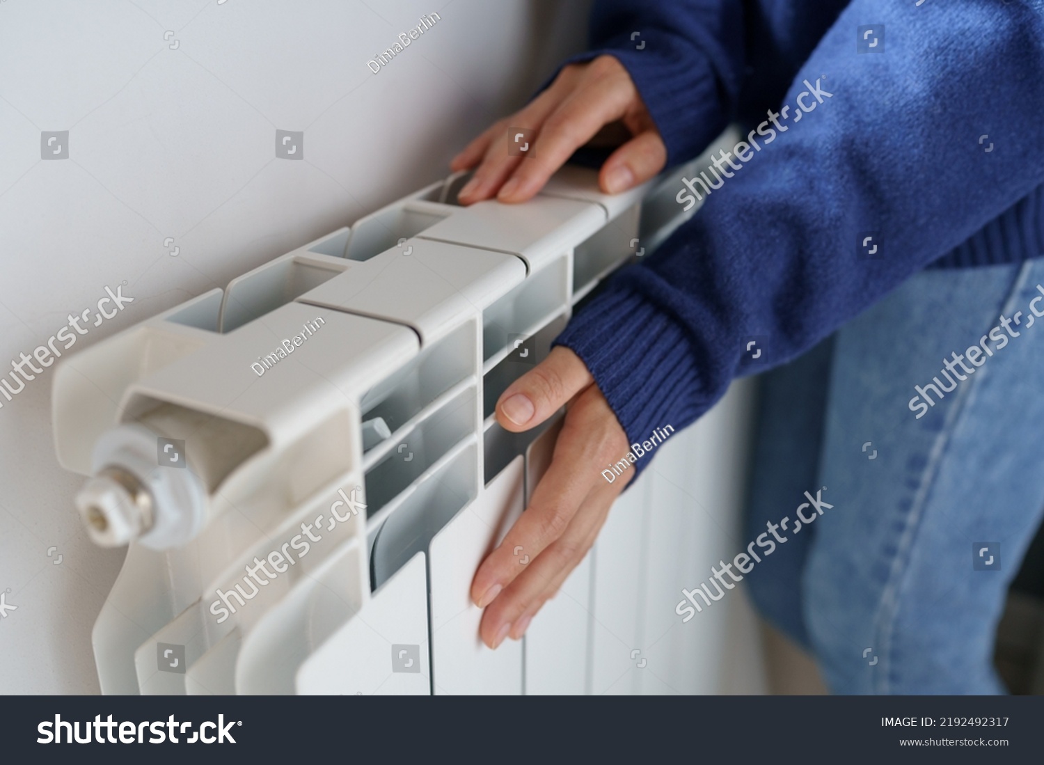 Closeup of woman warming her hands on the heater at home during cold winter days, top view. Female getting warm up her arms over radiator. Concept of heating season, cold weather.  #2192492317