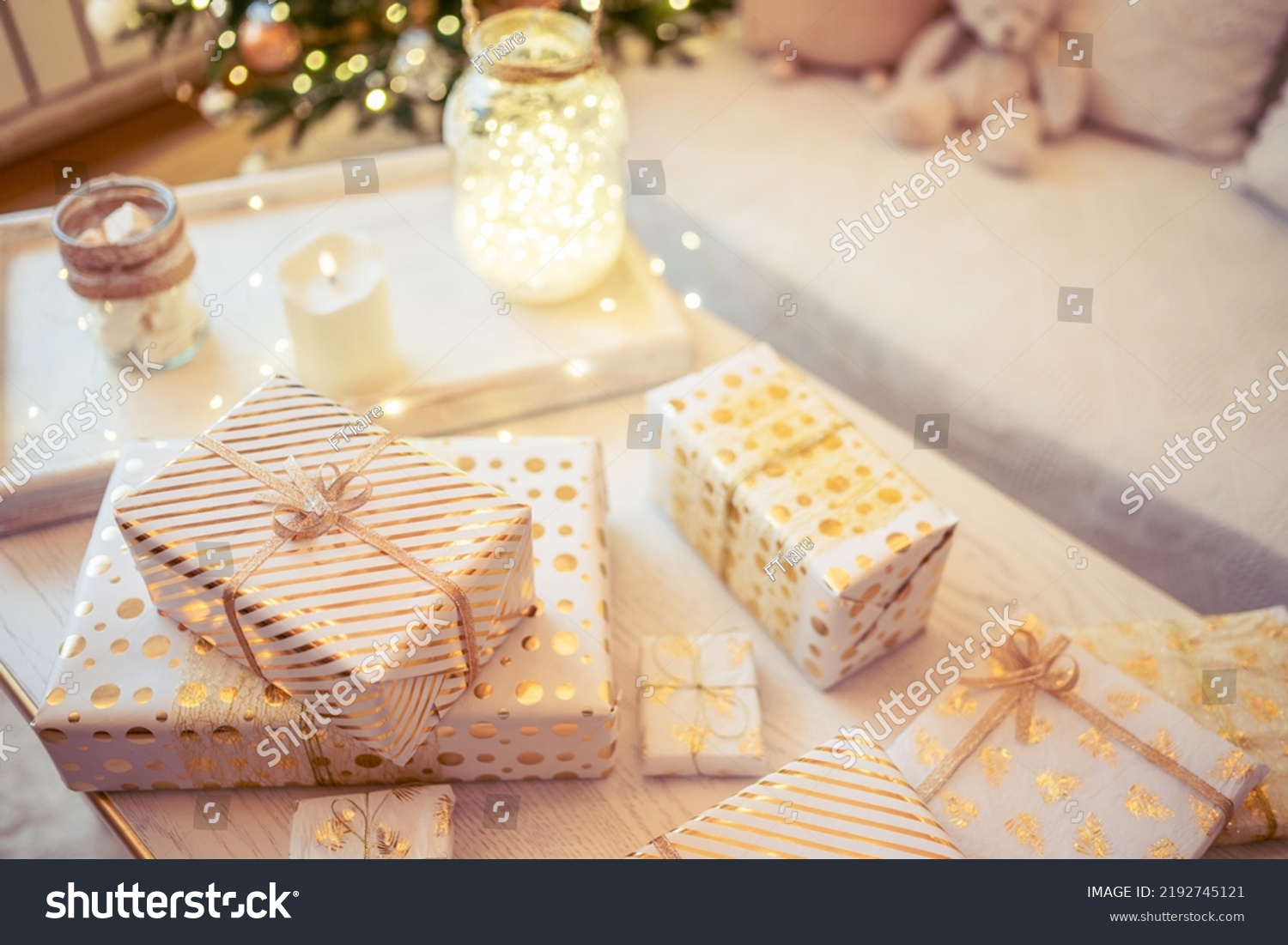 A lot of packing handmade gift boxes lying on the table near Christmas tree in the midst of golden lights, glowing garland, candle. Soft focus #2192745121