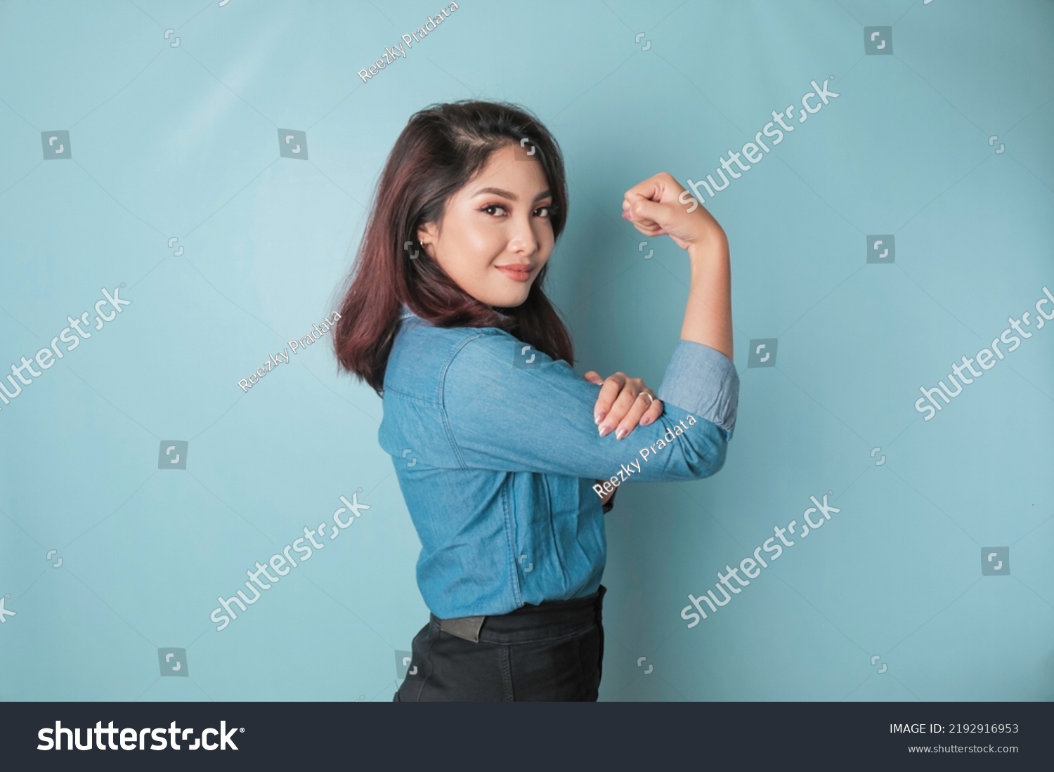 Excited Asian woman wearing a blue shirt showing strong gesture by lifting her arms and muscles smiling proudly #2192916953