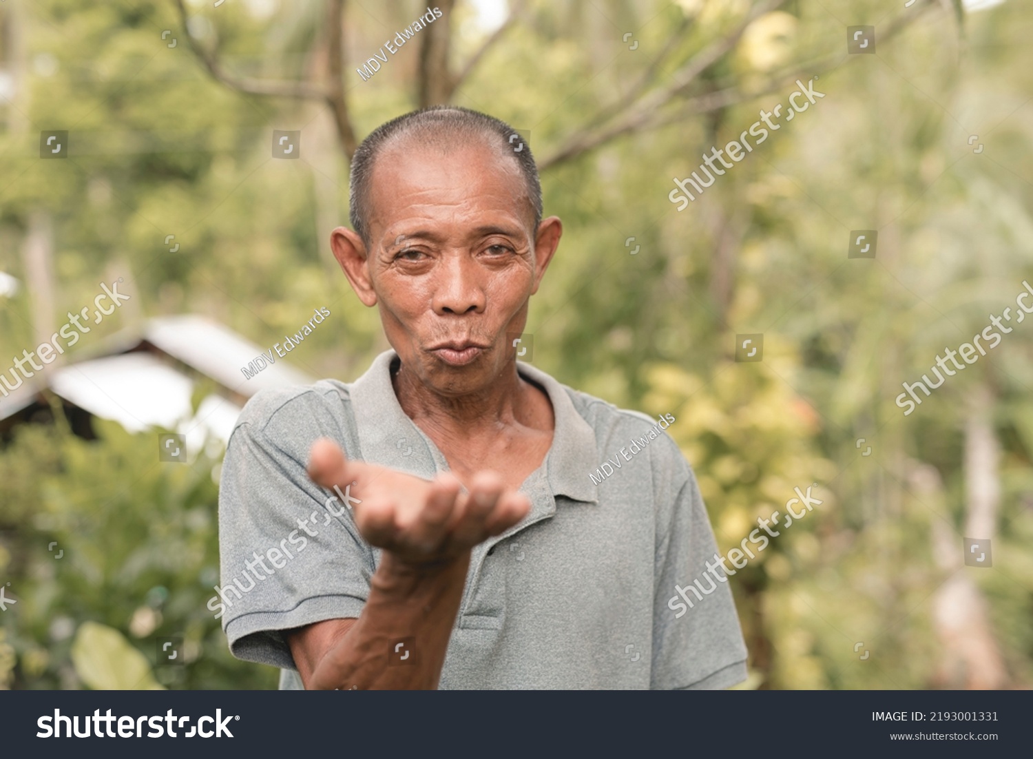 A funny old filipino man blows an imaginary kiss. Pursed lips signifying either a lighthearted gesture or catcalling. Outdoor scene. #2193001331