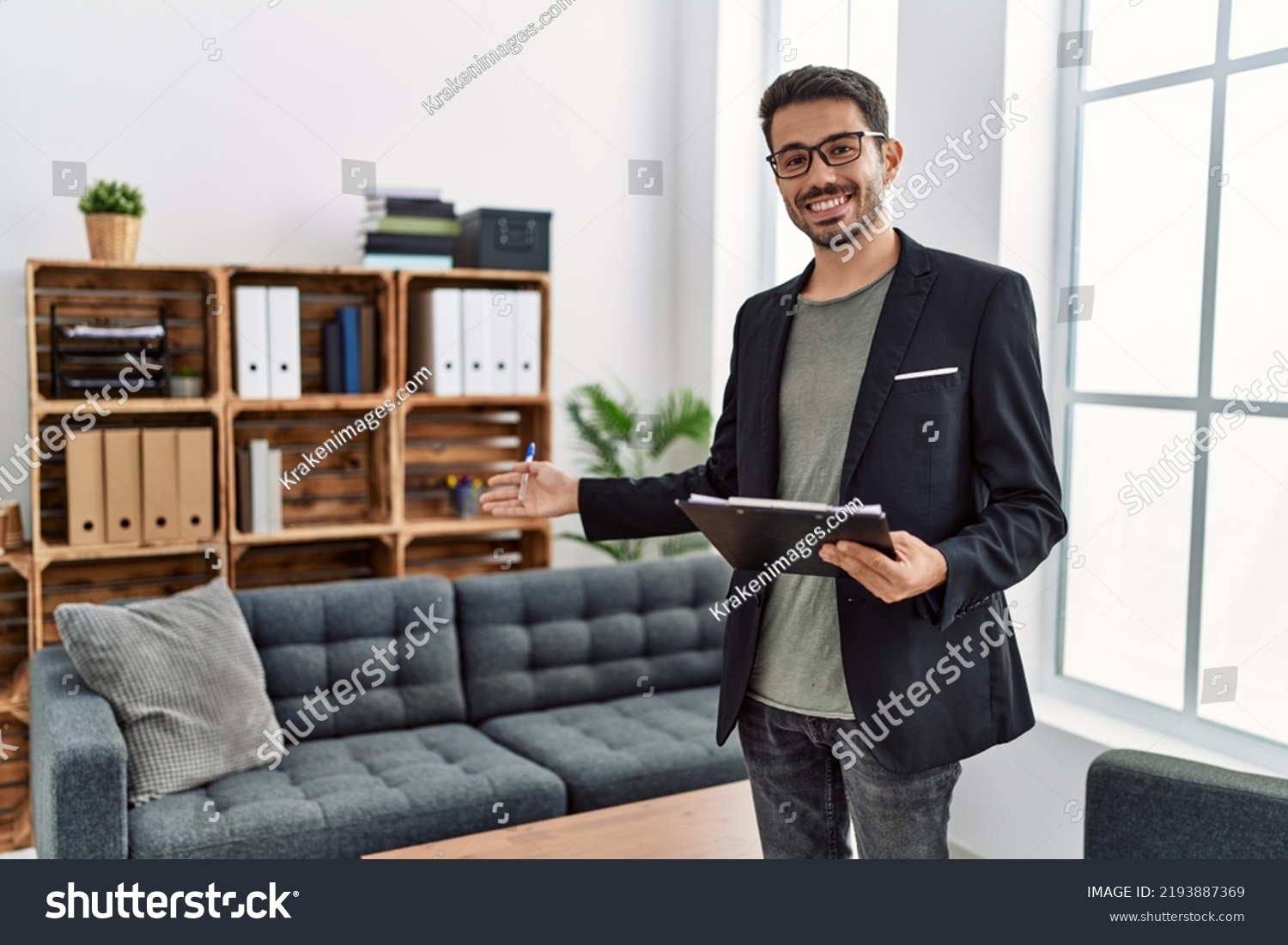 Young hispanic man having psychology session holding checklist welcoming patient at clinic #2193887369