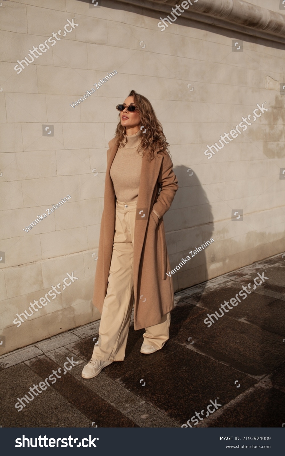 A style woman walking, enjoys a wonderful atmosphere of a vacation in fall time. The girl is wearing a urban beige sweater, sunglasses and resting against the background of the streets of the city #2193924089