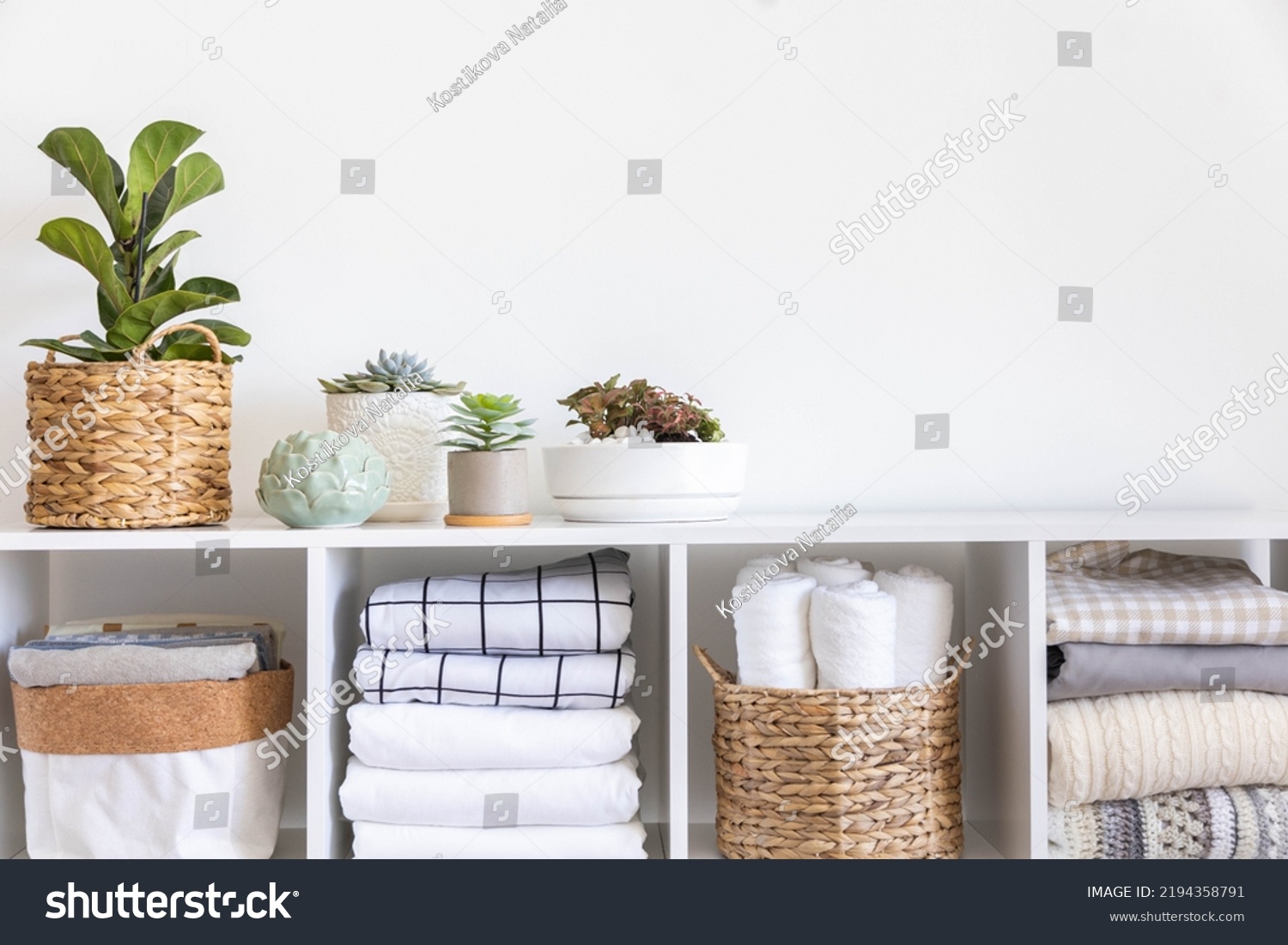 Potted plants in ecology straw baskets on shelf of bed linens cupboard textile arrangement storage organization. Minimalism Scandi placed method neatly folded cotton fabric bedding material copy space #2194358791