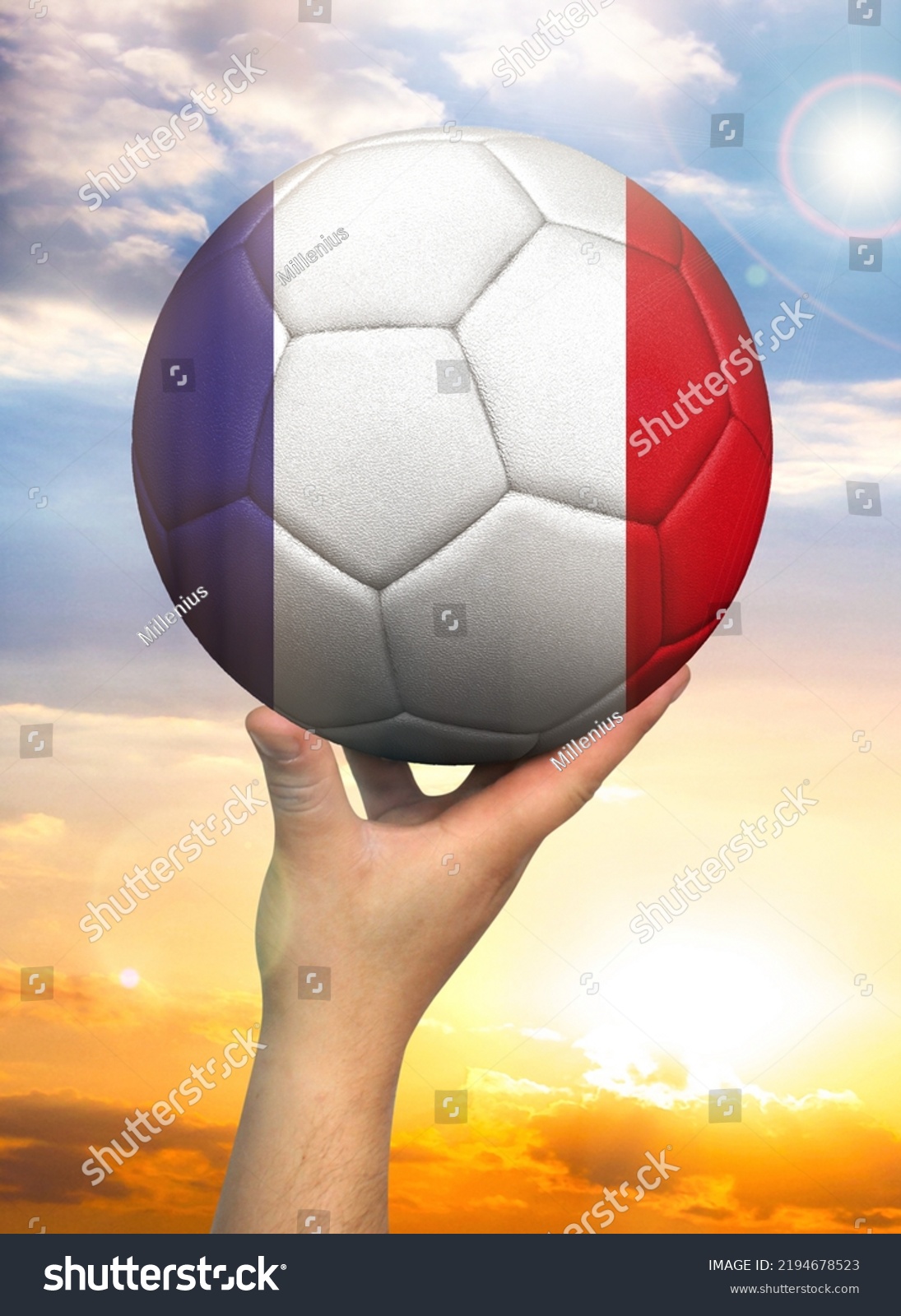Soccer ball in hand with a depiction of the flag of France against a colorful sky #2194678523