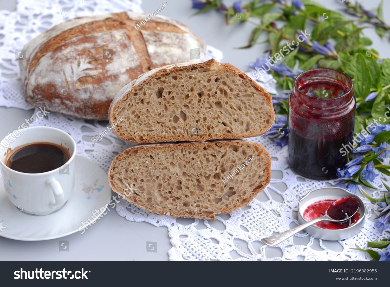 Bread texture of sliced dark bread loaf, cup of coffee and jam. Home baked wheat bread with rye flour and sesame seeds; two loafs of crusty sourdough wheat bread with rye flour; one loaf cut in half. #2196382955