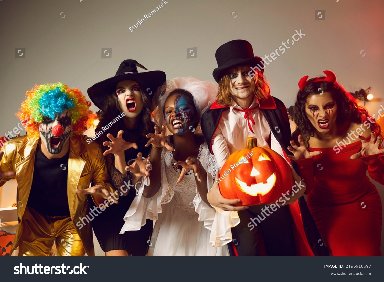 Group of young people dressed up as spooky characters having fun at Halloween costume party. Adult male and female friends with scary makeup on faces doing claw gesture, hissing and making grimaces #2196918697