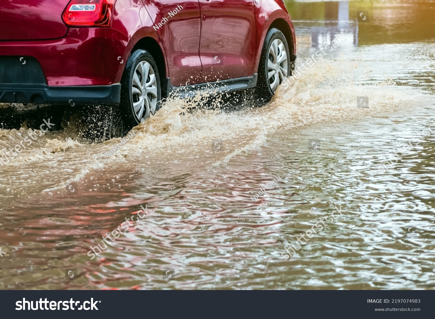 Car passing through a flooded road. Driving car on flooded road during flood caused by torrential rains. Flooded city road with a large puddle. Splash by car through flood water. Selective focus. #2197074983