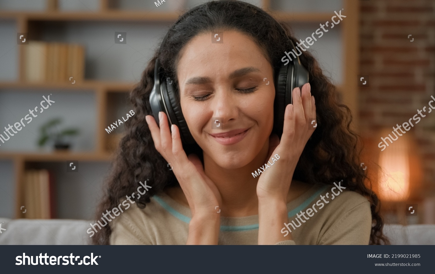 Front view close up smiling Hispanic woman with smiling enjoining lady relaxing at home with closed eyes listening to music in headphones audio sound song feeling well good mood hobby holiday indoors #2199021985