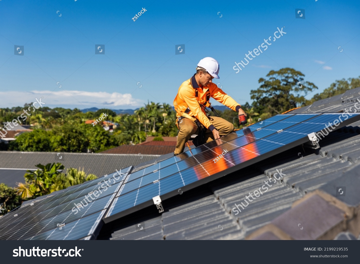 Solar panel technician with drill installing solar panels on house roof on a sunny day. #2199219535
