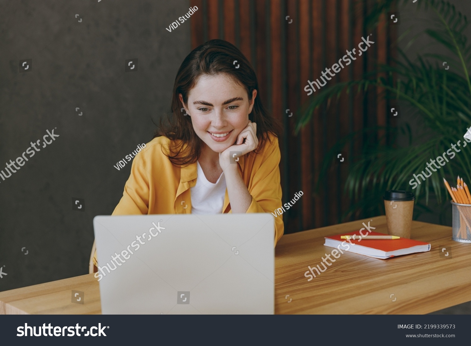 Young satisfied fun happy successful employee business woman 20s she wearing casual yellow shirt hold use laptop pc computer sit work at wooden office desk with pc laptop. Achievement career concept #2199339573