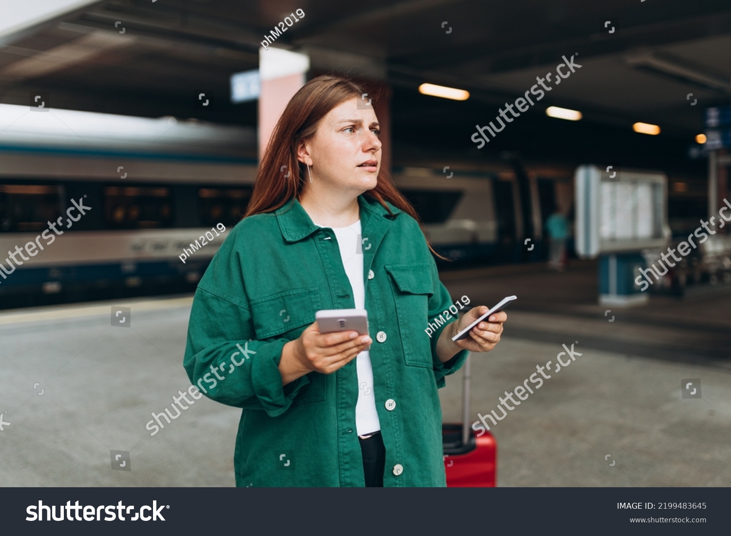 Young refugee redhhead woman crying and waiting train on station platform, she lost and using smart phone. Railroad transport concept, Traveler. #2199483645
