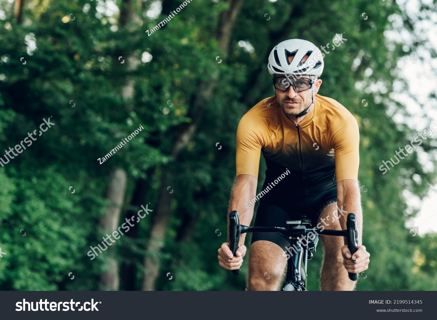 Sporty man wearing active wear and helmet riding a black bike in nature. Concept of people, workout and favorite hobby. Copy space. Looking into the camera. #2199514345