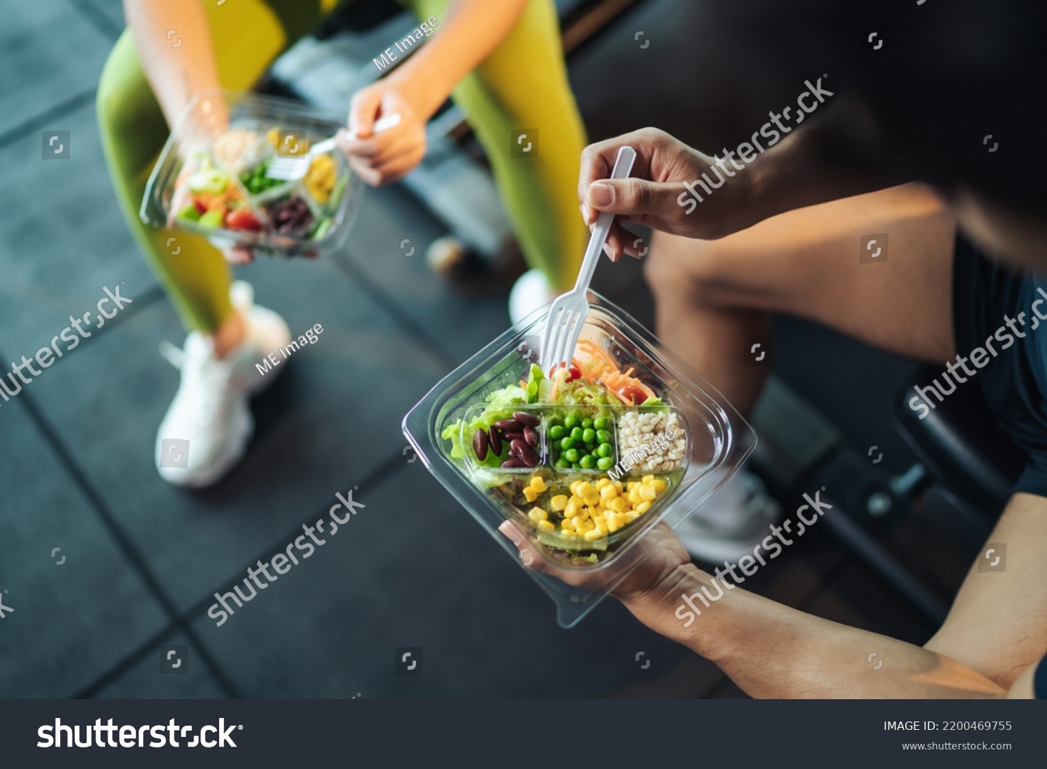 Top view Asian man and woman healthy eating salad after exercise at fitness gym. Two athlete eating salad for health together. Selective focus on salad bowl on hand. #2200469755