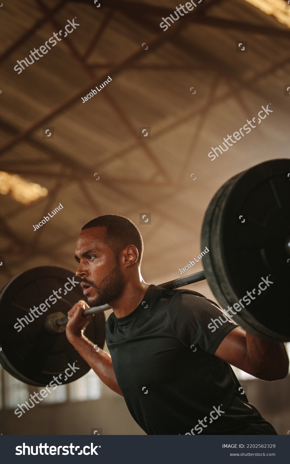 Fitness man doing back squats workout with heavy weight barbell. Sportsman doing exercise with heavy weights at old warehouse. #2202562329