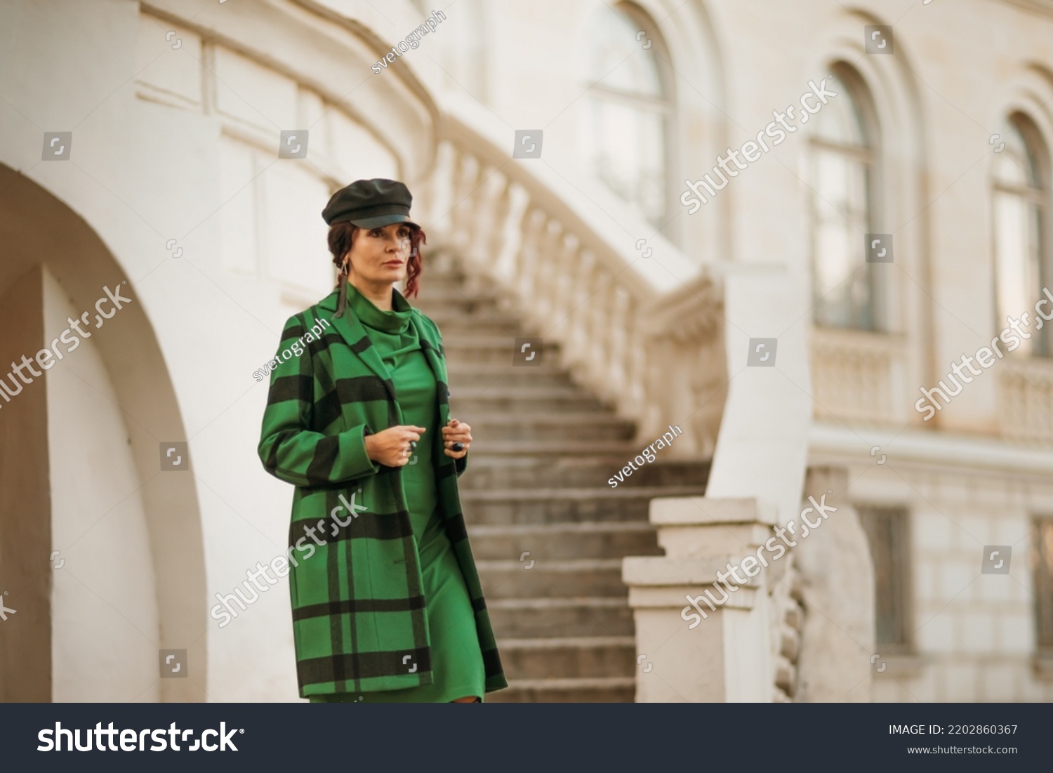 Outdoor fashion portrait of an elegant fashionable brunette woman, model in a stylish cap, green dress, posing at sunset in a European city in autumn. #2202860367