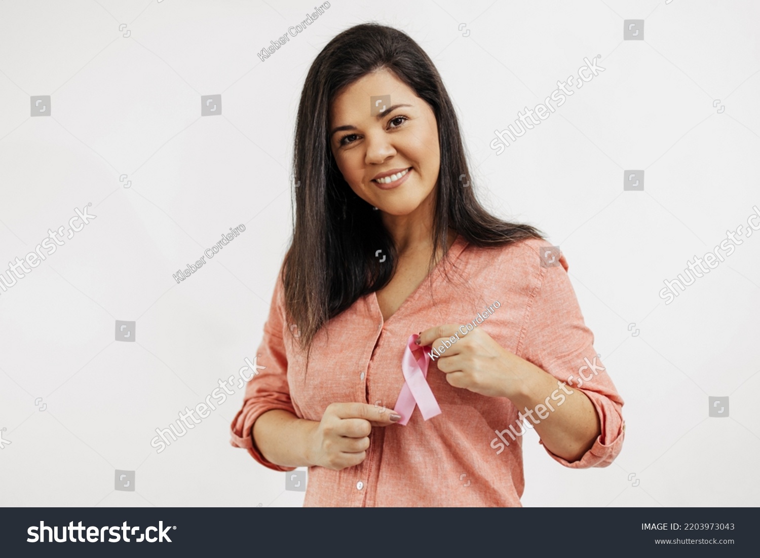 Young Brazilian woman holding breast cancer ribbon over white background #2203973043