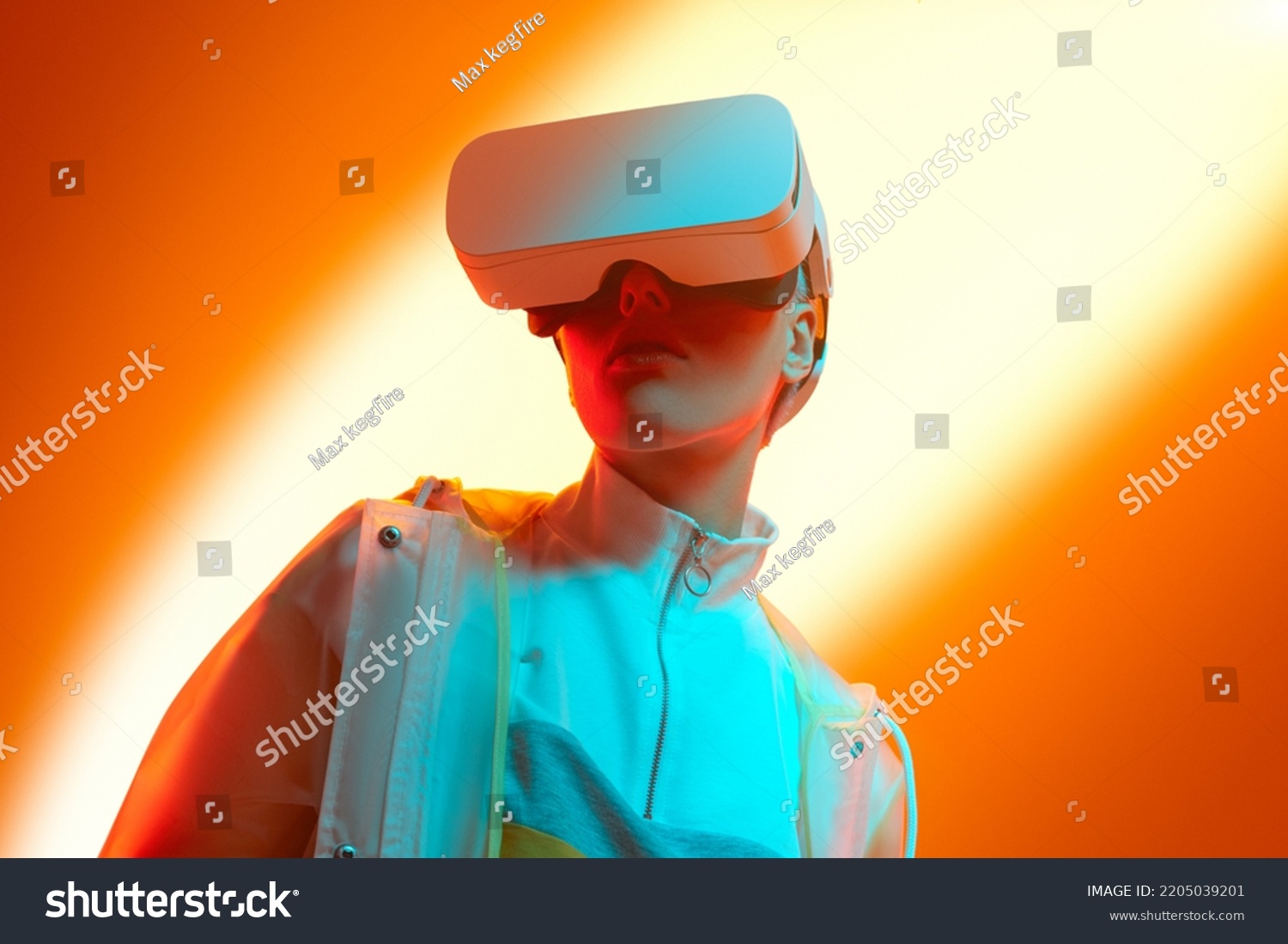 Low angle of young stylish woman in futuristic outfit and VR goggles exploring cyberspace against bright orange background in studio with neon illumination #2205039201