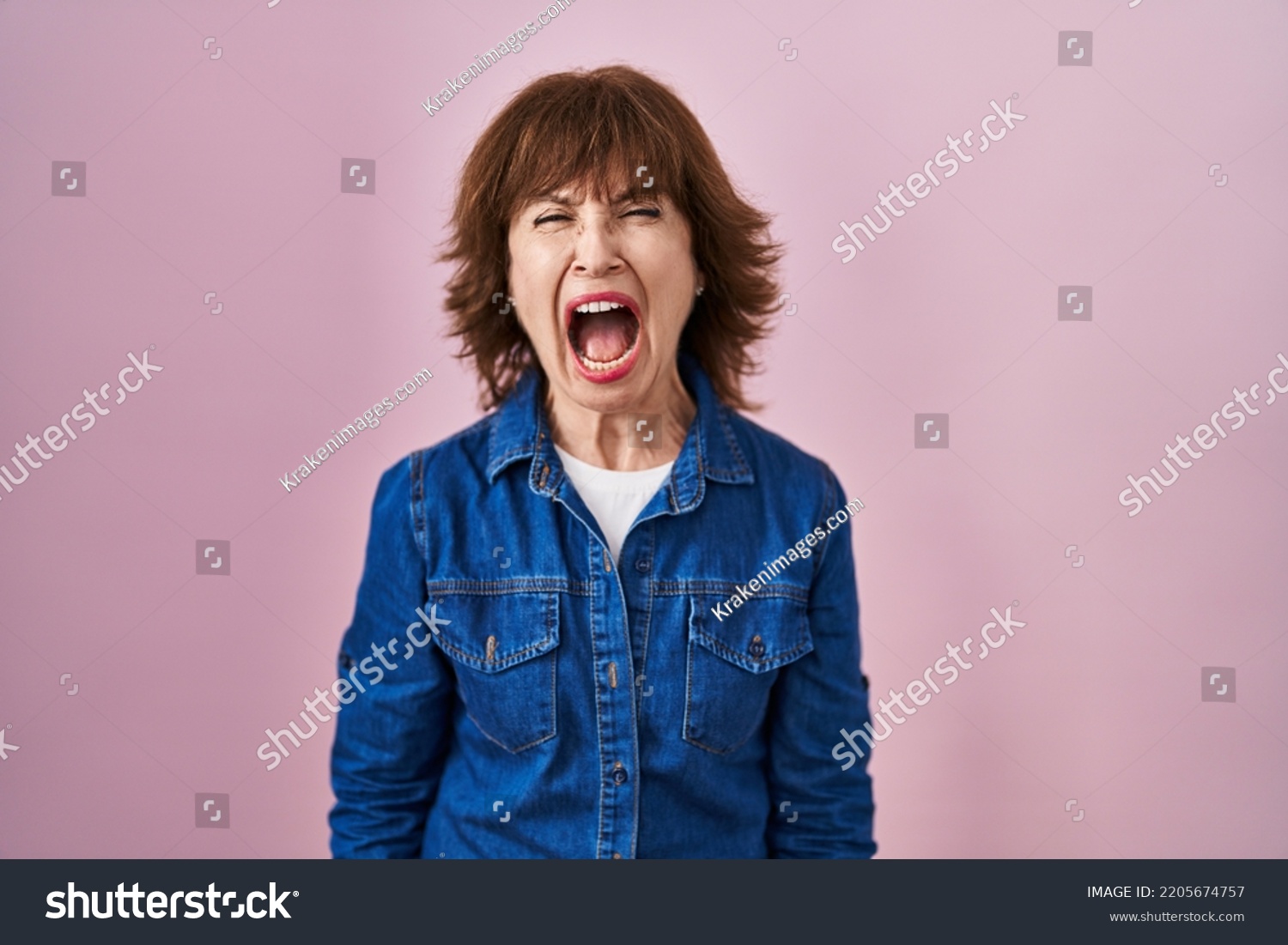 Middle age woman standing over pink background angry and mad screaming frustrated and furious, shouting with anger. rage and aggressive concept.  #2205674757
