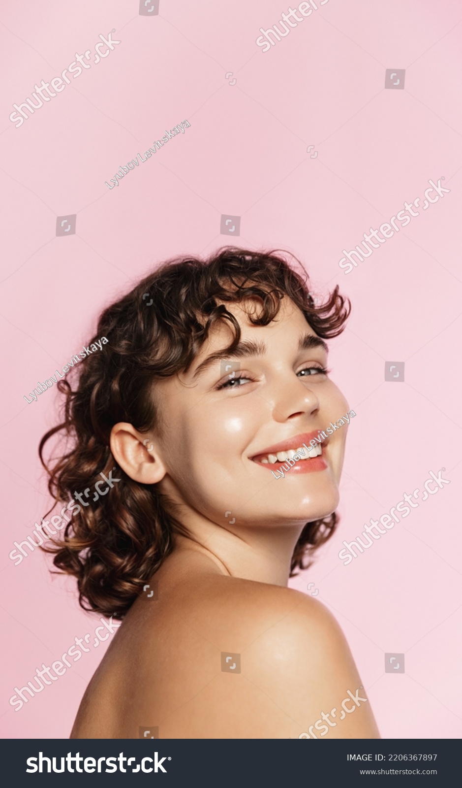 Skin care. Woman with beauty face and healthy facial skin portrait. Beautiful curly girl model with natural makeup touching glowing hydrated skin on pink background closeup. High quality image. #2206367897