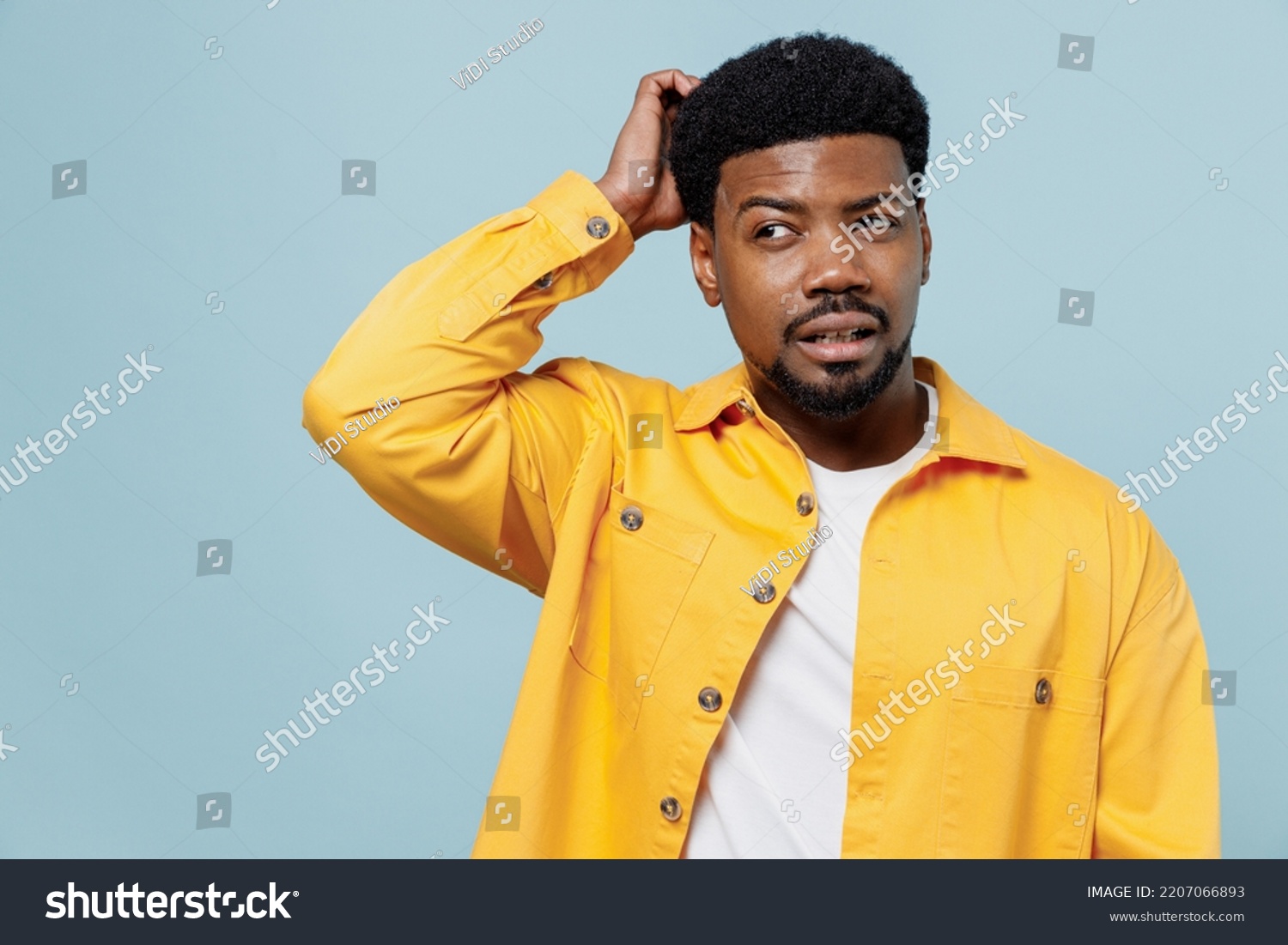 Young puzzled sad man of African American ethnicity wear yellow shirt look aside on workspace scratch hold head isolated on plain pastel light blue background studio portrait. People lifestyle concept #2207066893