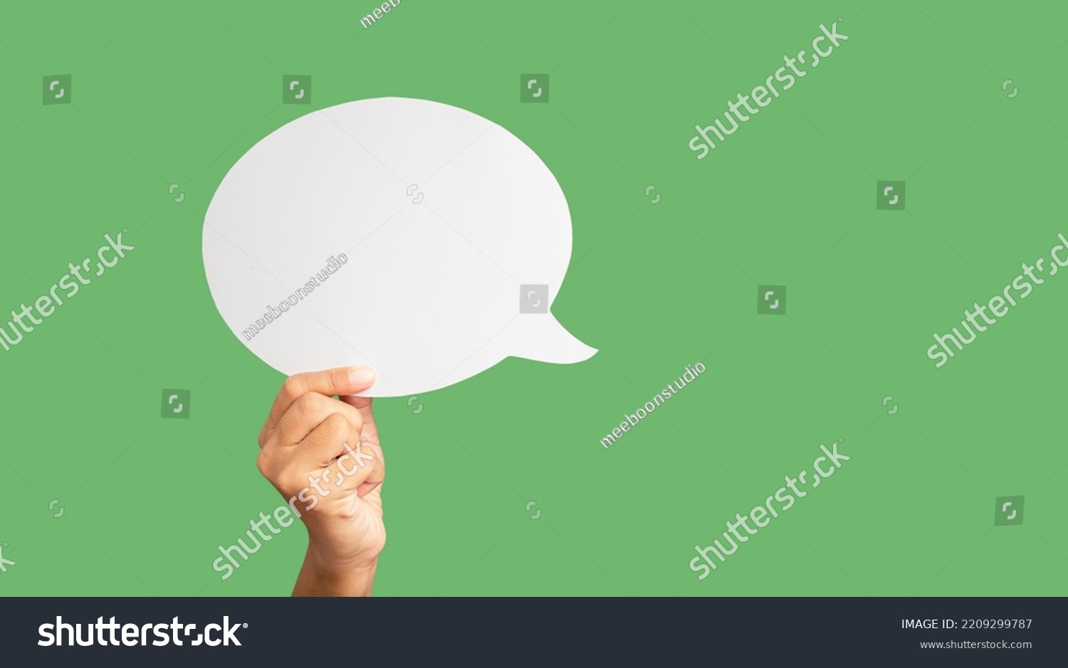 Close-up of hand holding a green speech bubble against a green background in the studio. Close-up photo. Space for text #2209299787