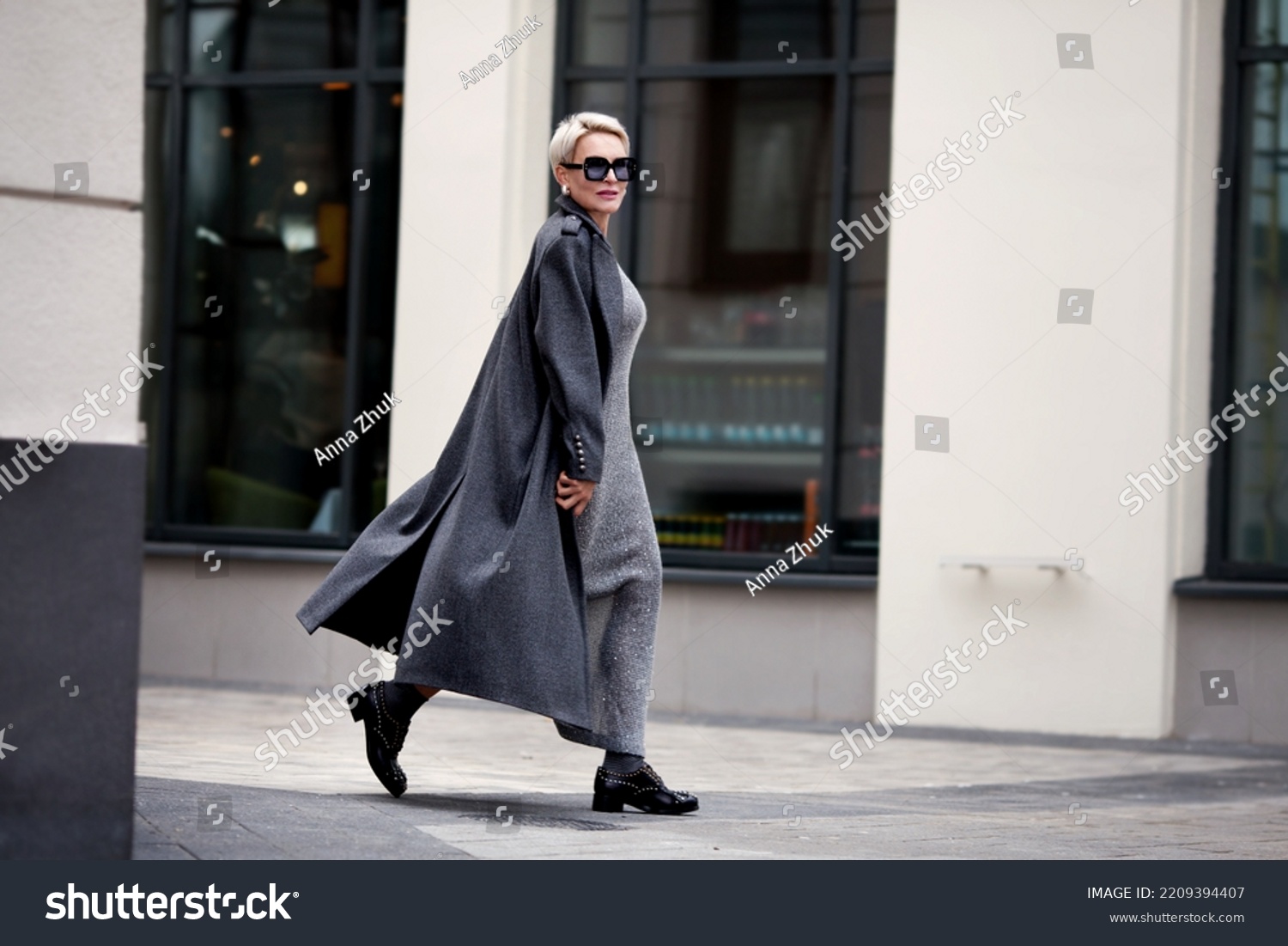 Elegant Mature woman walks city street , wears stylish clothes, gray wool coat, long dress, black shoes and glasses. Trending outfit #2209394407