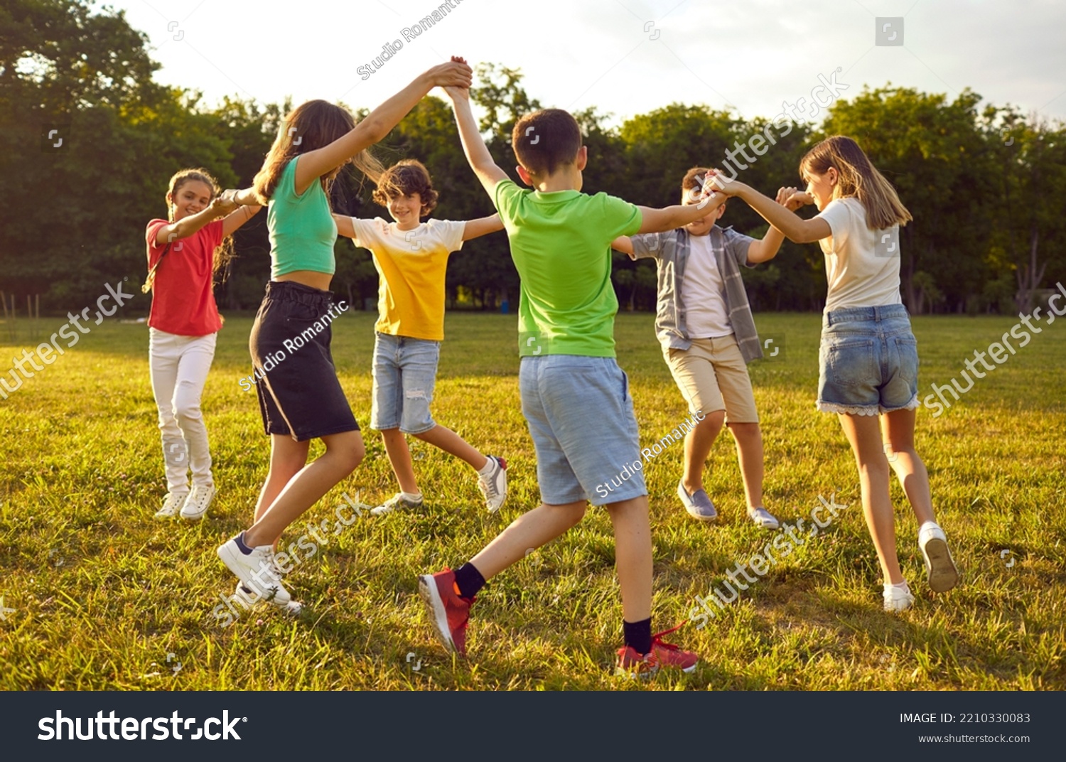 Group of kids playing games and having fun in nature. Joyful little children dancing a round dance on green grass in the park. Several happy little friends holding hands and running in a circle #2210330083