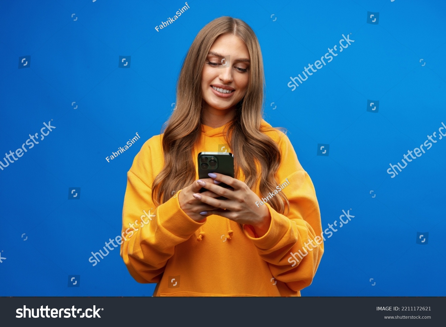 Portrait of young beautiful woman texting on the phone against blue background #2211172621