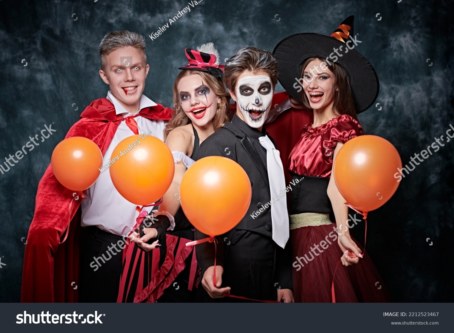 Merry Halloween party. Teenage friends in carnival costumes have fun celebrating Halloween. Skeleton, witch, clown and vampire. Studio portrait on vintage background. #2212523467