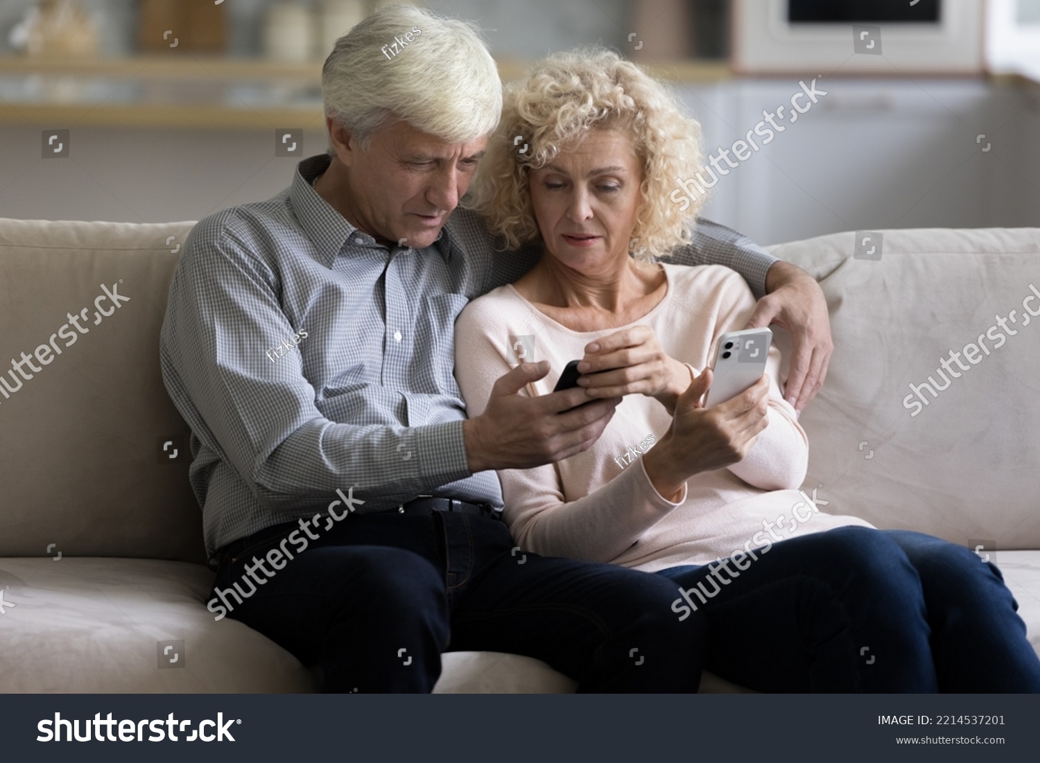 Serious elderly 70s couple sit on sofa hold two new bought modern smartphones, try to understand mobile application discussing software. Older generation use wireless gadgets, technology, lifestyle #2214537201
