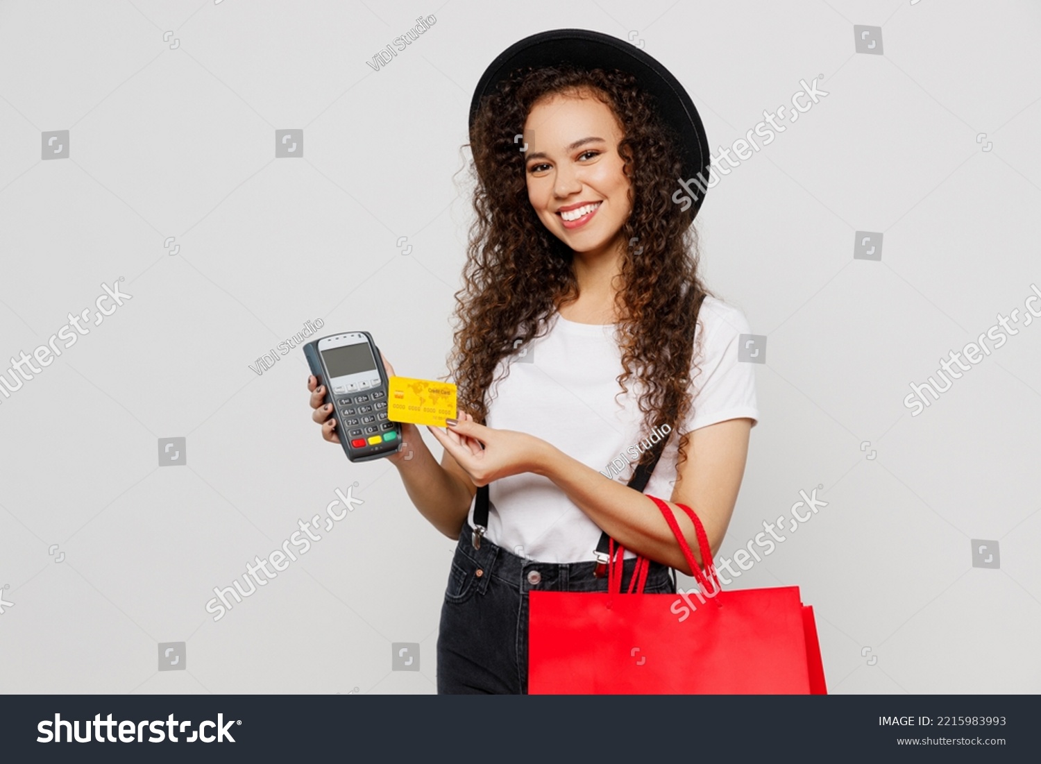 Young woman wear t-shirt hat hold red paper package bags after shopping bank payment terminal to process acquire credit card isolated on plain solid white background. Black Friday sale buy day concept #2215983993