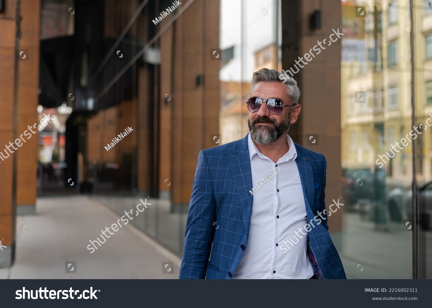 A handsome senior business man in glasses and a suit is walking through the city street near the office building. #2216002311