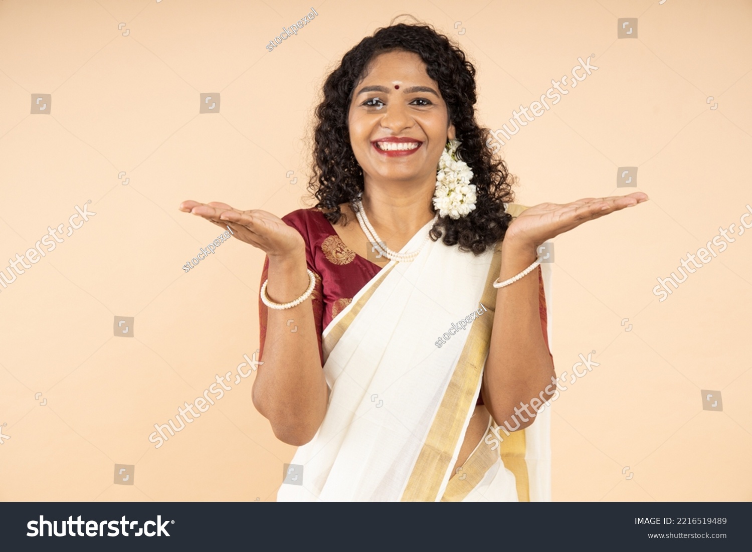Excited South Indian woman wearing traditional white saree with arms open gesture isolated on beige background, Advertisement and promotion #2216519489