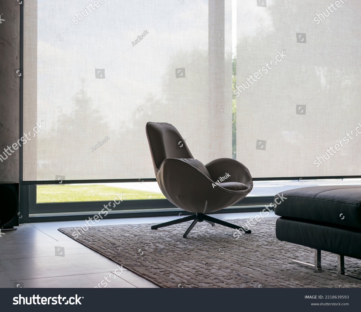 Roller blinds of large sizes on the window in the interior. Automatic solar shades, fabric with linen texture. In front of a large window is a chair on a carpet. Outside is a view of the garden. #2218639593