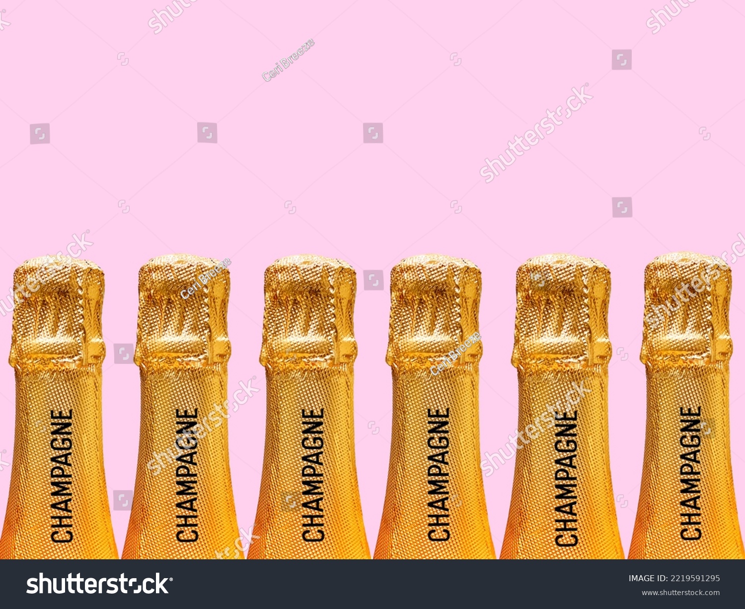 Row of champagne bottles covered in gold foil stamped with the word champagne on the neck against a plain pink background. No people. Copy space. #2219591295
