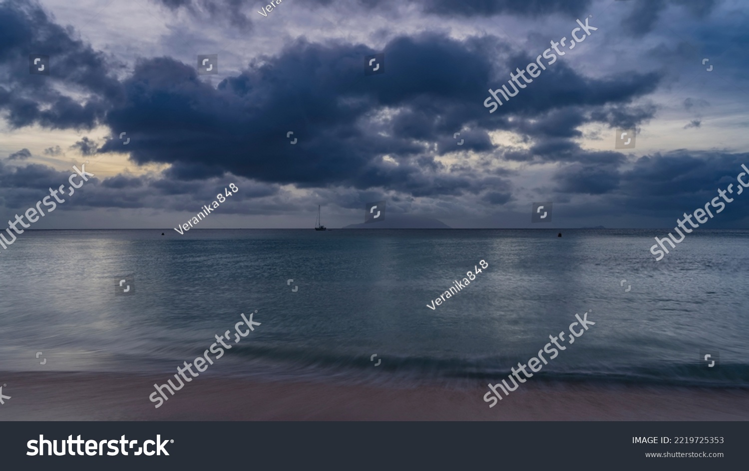 Evening twilight on a tropical island. Blue clouds in the sky. The turquoise ocean is calm. Waves on the sand, a yacht on the horizon. Seychelles. Mahe. Beau Vallon. Long exposure #2219725353