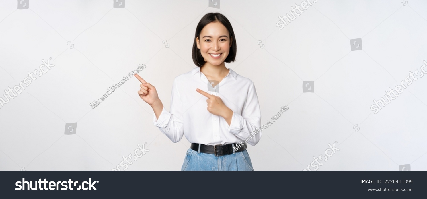 Image of smiling young office lady, asian business entrepreneur pointing fingers left, showing client info, chart of banner aside on copy space, white background. #2226411099