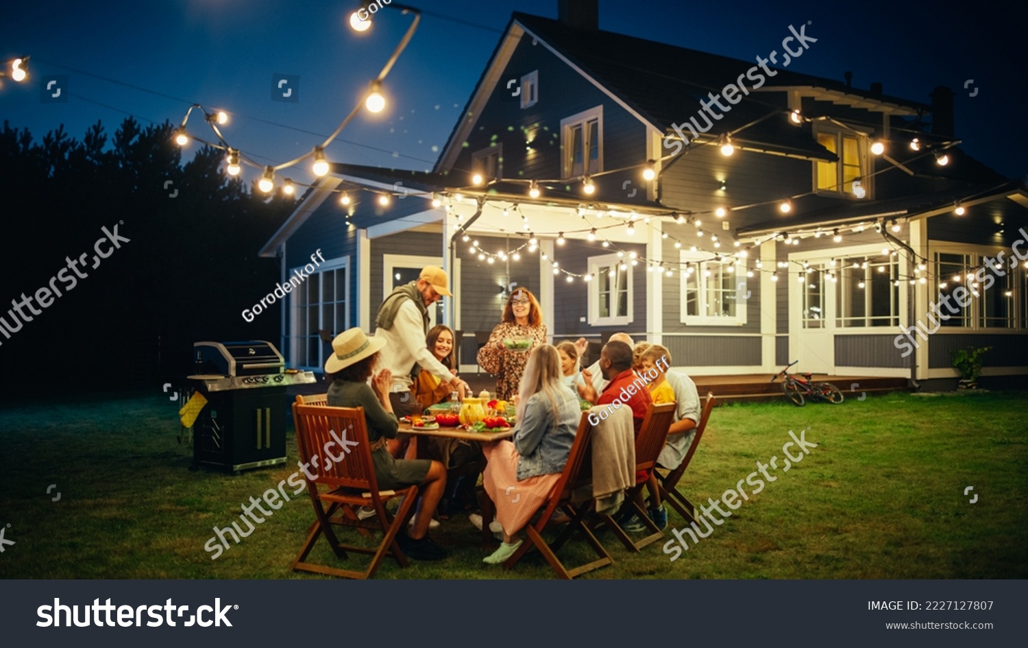 Group of Multiethnic Diverse People Having Fun, Sharing Stories with Each Other and Eating at Outdoors Dinner Party. Family and Friends Gathered Outside Their Home on a Warm Summer Evening. #2227127807