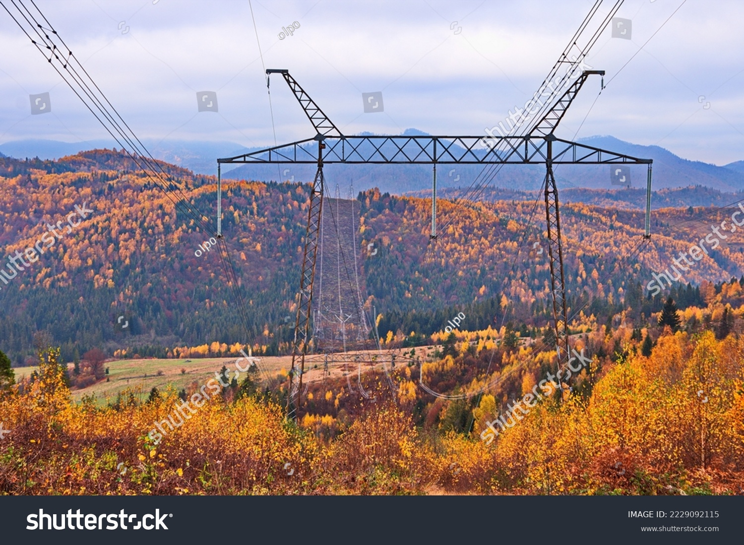 High voltage electric transmission pylon. Electricity transmission pylon against autumn forest on mountain slops in Ukrainian Carpathians. High voltage electric tower. #2229092115